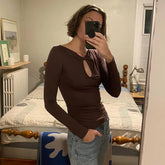Person taking a mirror selfie wearing a brown long-sleeve top with a cutout design and blue jeans in a bedroom.
